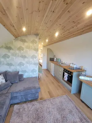a living room with a couch and a kitchen at The Galloway Steading -The Hedgehog's Hideout family cabin with Hot Tub and Fire Pit in Glenluce