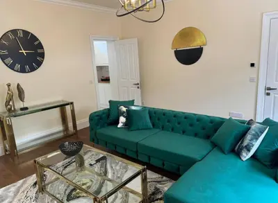a living room with a green couch and a clock at Glasgow Central Paradise - Spacious 3- Bed House in Glasgow
