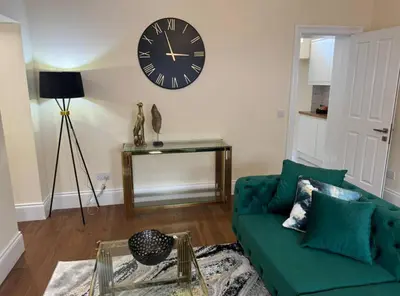 a living room with a green couch and a clock on the wall at Glasgow Central Paradise - Spacious 3- Bed House in Glasgow