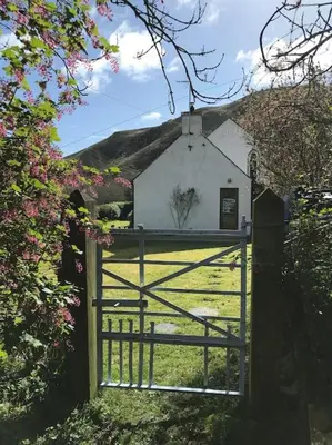 an open gate to a small white building with a fence at Coolranny Schoolhouse in Torr
