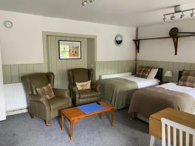 a room with two beds and a chair and a table at The Bothy at Christmas Cottage in Rowardennan
