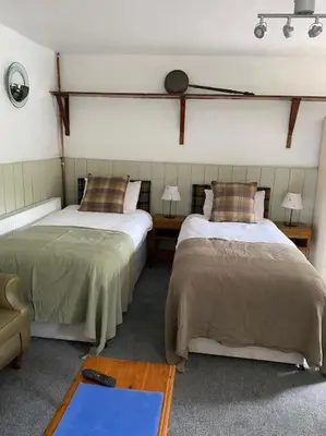 a room with two beds and a chair and two tables at The Bothy at Christmas Cottage in Rowardennan