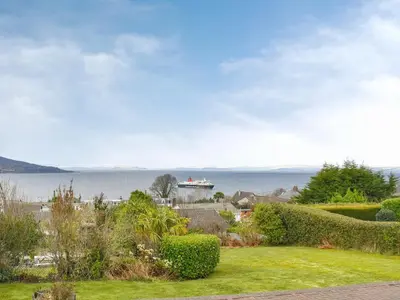 a house with a garden with a boat in the water at The Willows in Brodick