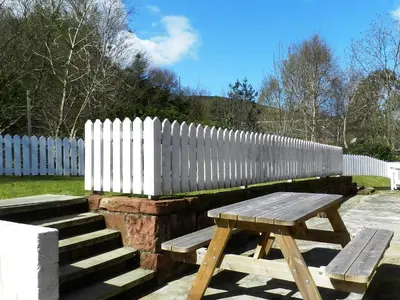 a wooden picnic table next to a white fence at Craigard Cottage in Corrie