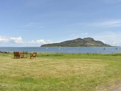 a table and chairs sitting on the grass near the water at Kinneil Land in Lamlash