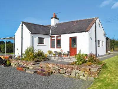 a white house with a table and chairs in front of it at Beuchan Cottage Keir Mill in Closeburn