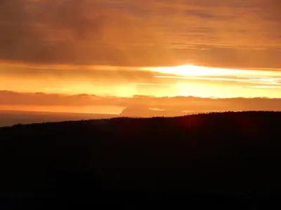 a sunset with the sun setting over the ocean at Hazel's Cottage in Campbeltown