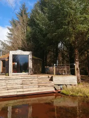 a wooden dock with a building on the water at Otter - Eco Bothy with Hot Tub in Castle Douglas