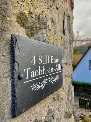 a sign on the side of a stone wall at Loch Lomond 2 Bedroom Apartment in Tarbet