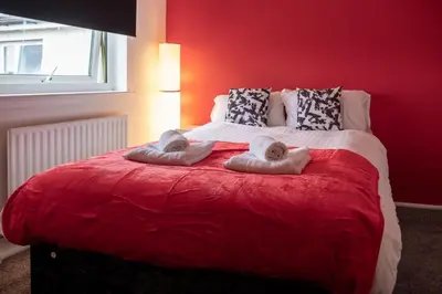 a red bedroom with a bed with towels on it at 2 Bedroom Beautiful Apartment in Motherwell in Mossend