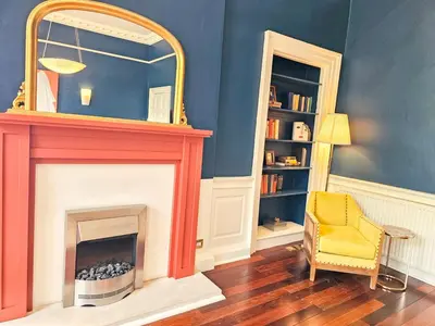 a room with a fireplace with a mirror and a chair at Spacious 2 Bedroom Apartment in the heart of New Town in Edinburgh
