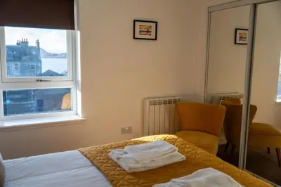 a bedroom with a bed and a chair and a window at Aberlour Apartment in Oban