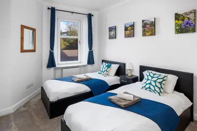 two beds in a room with blue curtains at Oban Bay Views - Fireplace, Games & Books in Oban