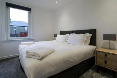 a bedroom with a bed with white sheets and a window at Marchfield Promenade View in Prestwick