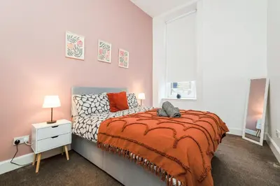 a bedroom with a bed with an orange blanket at 4 Beds - City Gateway Getaway with Free Parking in Glasgow