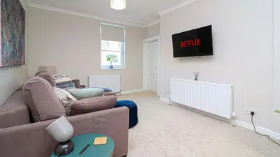 a living room with a couch and a tv on the wall at Modern And Cozy Apex Apartment in Helensburgh