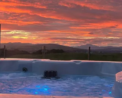 a hot tub with a sunset in the background at Arrochar View in Langbank