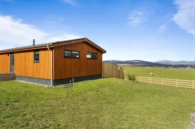 a wooden house on a field with a fence at Arrochar View in Langbank