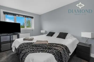 a bedroom with a large bed and a flat screen tv at Brand New 4 Bedroom House - Sleeps 4 Fully Equipped, Free Parking, WiFi, Perfect for CONTRACTORS by Diamond Short Lets in Rosyth