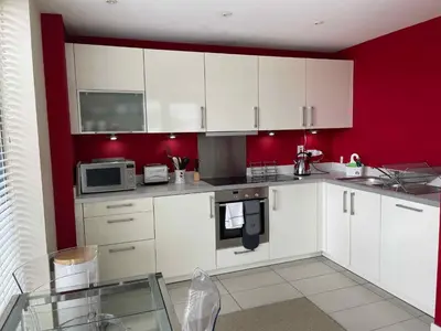a kitchen with white cabinets and a red wall at Glasgow Harbour River West End in Glasgow