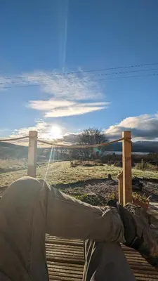 a person laying on a wooden deck looking at a field at Otter Burn Cabin in Oban
