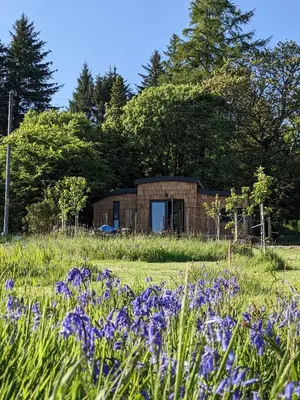 a brick building in a field with purple flowers at Otter Burn Cabin in Oban