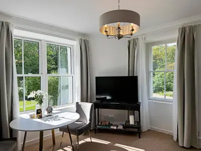 a living room with a table and a tv and windows at The Garden Flat in Fort William