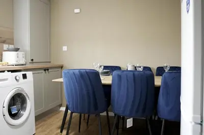 a dining room table with blue chairs and a washing machine at Barclay House in Livingston
