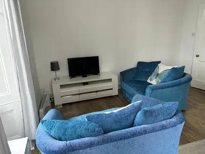 a living room with two blue chairs and a tv at Our Wee Eden - Rothesay in Rothesay