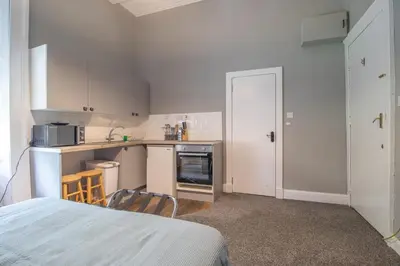 a kitchen with white cabinets and a bed in a room at Cosy Palm Studio West End - Pass the Keys in Glasgow