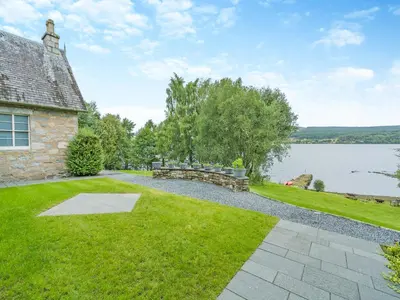 a stone house with a grassy yard next to a lake at Uk47813 - Cooks Cottage in Kinloch Rannoch