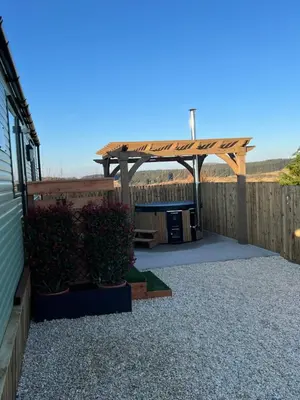 a backyard with a wooden pergola and some bushes at Maneight Fir View with hot tub in Dalleagles