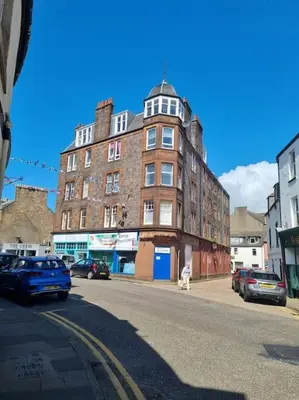 a large brick building on a city street with parked cars at Mafeking Place Apartment in Campbeltown