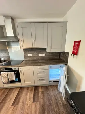a kitchen with white cabinets and a wooden floor at Inchcruin Apartment - Macaulay Letting in Bonhill