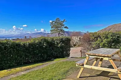 a wooden picnic table in the grass with mountains in the background at 1 Bedroom Cabin with Mountain & Loch Views - Quiet Location between Glencoe & Ben Nevis in Corran