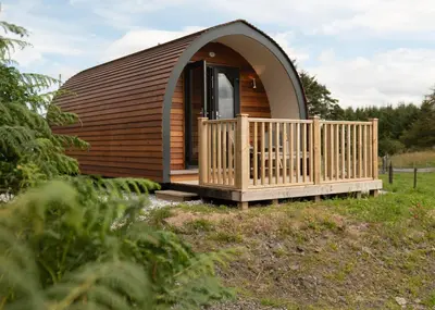 a circular cabin with a wooden porch and a deck at Countryside Farm Pod on Isle of Seil - B in Balvicar