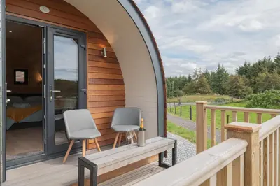 a wooden house with two chairs on a deck at Countryside Farm Pod on Isle of Seil - B in Balvicar