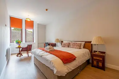 a bedroom with a large bed and a table and chairs at The Hazlitt Apartments in Paisley