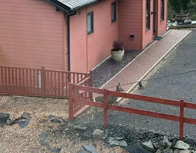 a red house with a fence in front of it at Ghillie's Croft Cabin, Rothesay in Rothesay