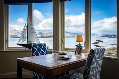 a wooden table with a sail boat in a room with windows at The Pierhouse Hotel in Port Appin