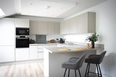 a white kitchen with white cabinets and two bar stools at Penthouse Apartment at Loch Lomond with 2 bedrooms in Balloch