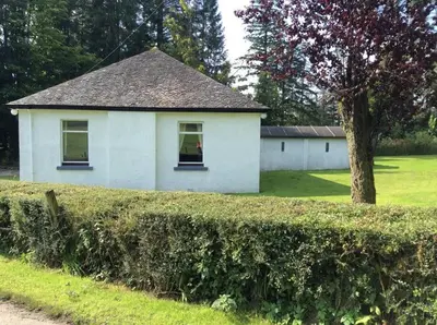 a white house with a tree in a field at Lednabra Cottage in Drymen