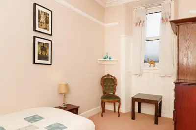 a bedroom with a bed and a chair and a window at Garmoyle House & Garmoyle Mid Cottage in Dumbarton