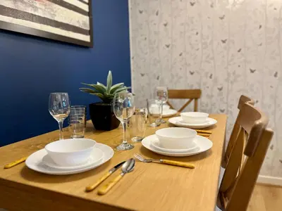 a wooden table with plates and wine glasses on it at Ground Floor Flat with Free Parking & WiFi in Glasgow