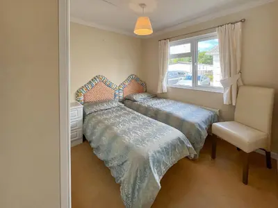 a bedroom with two beds and a chair and a window at Tredegar in Newton Stewart