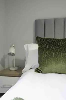a bed with a green pillow and a lamp at Pentland House in Bathgate