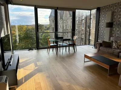 a living room with a table and chairs and large windows at Stunning park view Quartermile apartment close proximity to Castle University in Edinburgh