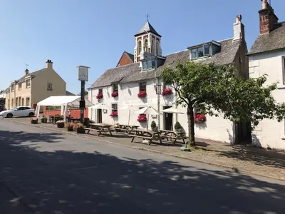 a white building with benches on the side of a street at The Cross Keys in Kippen in Kippen