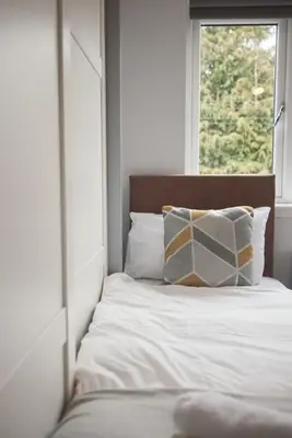 a bed with white sheets and pillows in front of a window at A stunning And Slick Escape in Stonehouse
