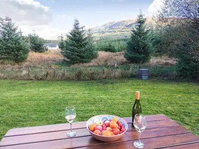 a table with a bowl of fruit and a bottle of wine at Pine Cottage in Killin